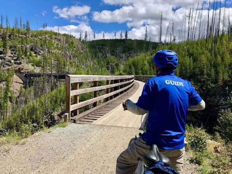 Cyclists crossing a historic wooden trestle bridge in Myra Canyon Kelowna on a full-day bike and wine tasting tour in the Okanagan